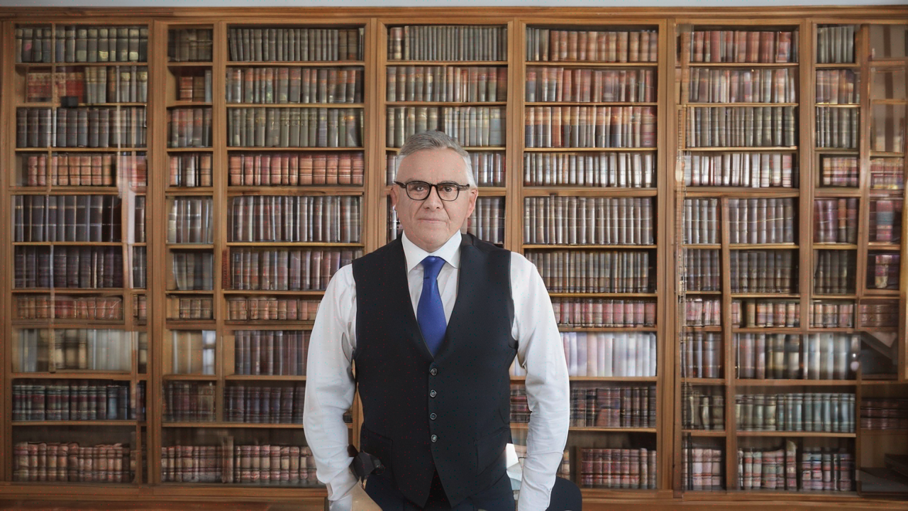 Portret Adama Nowaka, mężczyzny z brodą w okularach, stojącego przy regale z książkami w domowej bibliotece