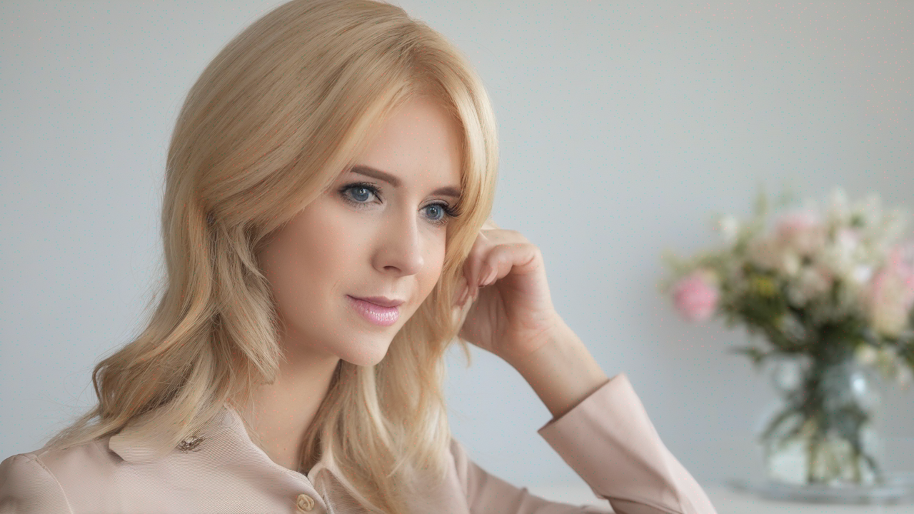 Uśmiechnięta kobieta w średnim wieku z okularami i krótkim blond bobem, ubrana w elegancką bluzkę